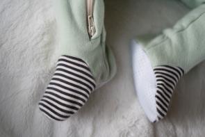 Close up image of baby feet in a mint colored footie with grey and natural pin striped fabric over the toe area. End of natural colored zipper is also showing on one leg.